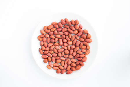 Crude red peanuts on a plate on a white background