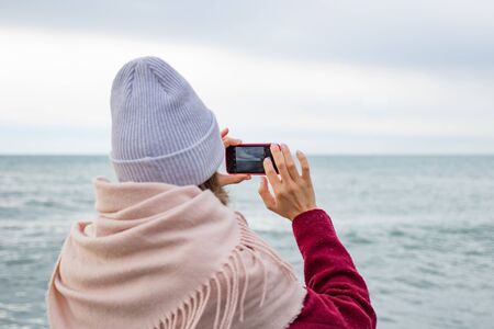 Girl in a hat photographs the sea on a smartphone