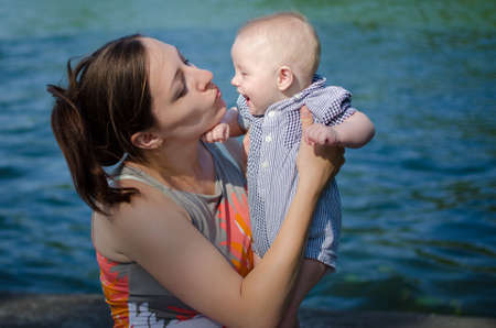 Mother kisses her little son on background of waterの写真素材
