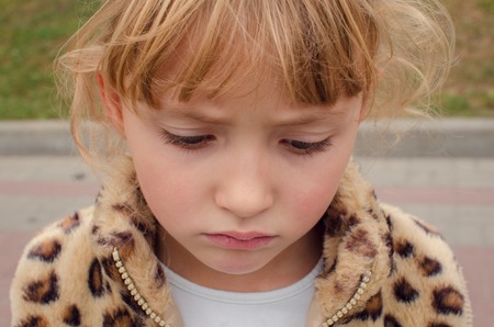 Portrait of a beautiful sad little girl with long lashes looking down, close-upの写真素材