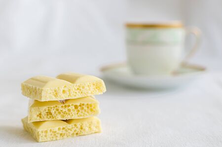 Heap of aerated porous white chocolate bars with cup of coffee on a white background.の写真素材