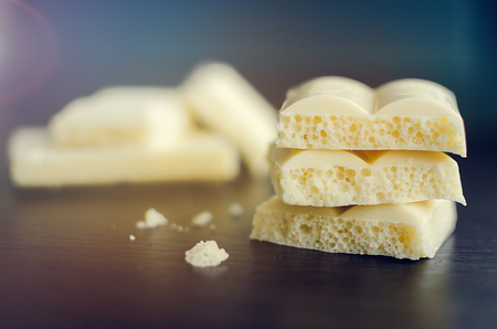 Heap of aerated porous white chocolate bars on dark wooden background. Tasty bubble milk chocolate bar. Selective focus, closeup, horizontal. Toned image.の写真素材