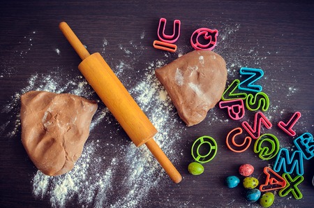 Easter baking preparation. Raw dough, rolling pin and cutters for the holiday cookies on a dark wooden table. Easter eggs. Easter food concept. Top view.の写真素材