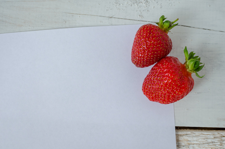 Red berry strawberry on white wooden background with sheet of paper. Background from freshly harvested strawberries with space for text. Strawberry background. Directly above. Top view. Copy space.の写真素材
