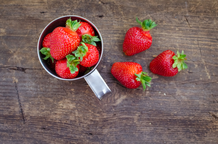 Red berry strawberry in metal mug on old rustic wooden background. Background from freshly harvested strawberries. Strawberry background. Directly above. Top view. Horizontal.の写真素材
