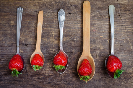 Succulent juicy fresh ripe red strawberries on vintage metal and wooden spoons over old rustic wooden table top. Agriculture, Gardening, Harvest Concept. Top view.の写真素材