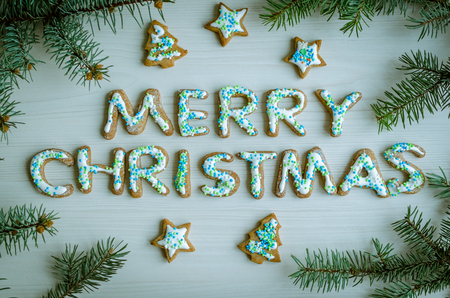 Wording Merry Christmas from homemade gingerbread cookies with icing on white wooden background with fir tree. Christmas concept. Christmas moody style greetings card. Happy New Year. Top view.の写真素材
