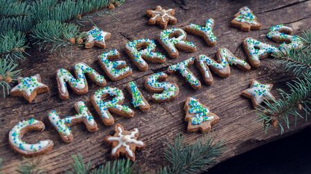 Wording Merry Christmas from homemade gingerbread cookies with icing on old wooden background with fir tree. Christmas moody style greetings card. Happy New Year. Christmas concept. Selective focus.の写真素材