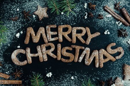 Phraze Merry Christmas from homemade gingerbread cookies, fir tree, cinnamon and anise on chalkboard background. Merry Christmas and Happy New Year. Xmas concept. Top view.の写真素材
