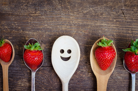 Strawberries on spoons and wooden spoon with smiley face. Leadership, uniqueness, independence, initiative, strategy, dissent, think different, success, summer, happiness, smile, positivity concept.の写真素材