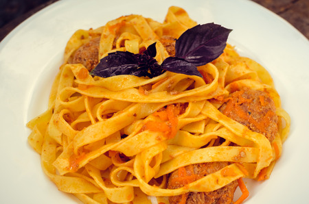 Tagliatelle with meatballs on wooden background. Traditional Italian pasta with a spicy tomato based meat sauce garnished with fresh basil. Top view. Close up.の写真素材