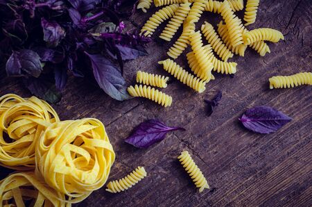 Fusilli and tagliatelle with fresh purple basil on old rustic wooden background. Traditional Italian pasta. Top view.の写真素材