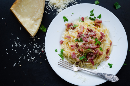 Pasta Carbonara. Spaghetti with bacon, parsel and parmesan cheese. Pasta Carbonara on white plate with parmesan on dark background. Italian food concept. Top view.の写真素材