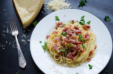 Pasta Carbonara. Spaghetti with bacon, parsel and parmesan cheese. Pasta Carbonara on white plate with parmesan on dark background. Italian food concept. Top view.の写真素材