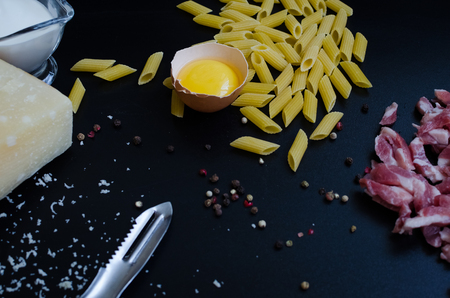 Ingredients for Pasta Carbonara on dark background. Set of products for pasta Carbonara - pasta, bacon, cream, Parmesan cheese, egg. Italian food concept. Selective focus.の写真素材