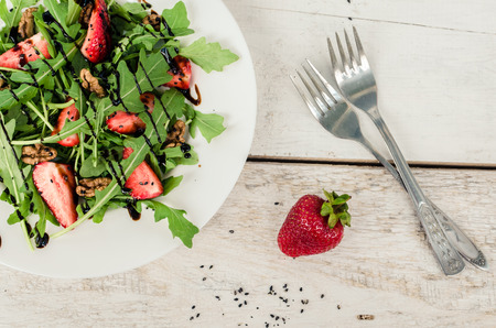 Fresh salad with arugula, strawberries, nuts, black sesame seeds and balsamic glasse sauce served on white plate on rustic wooden table. Healthy organic diet food concept. Top view.の写真素材