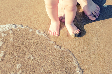 Toddler baby doing his first steps on the beach. Bare feet father and son staying on the sand near the bank in sunny day. Summertime holidays concept. Top view. Copy space.の写真素材