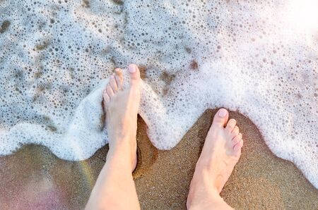 Feet of a young woman touching water on tropical beach in sunny summer day. Vacation holidays...