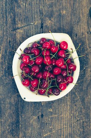 Red ripe juicy cherry in metal plate on rustic wooden background. Sweet summer berries. Freshly harvested merry. Directly above. Top view. Copy space.の写真素材