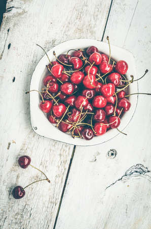 Red ripe juicy cherry in metal plate on white rustic wooden background. Sweet summer berries. Freshly harvested merry. Directly above. Top view. Copy space.の写真素材