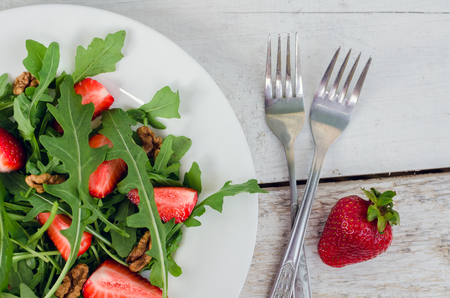 Fresh salad with arugula, strawberries and nuts served on white plate on rustic wooden table. Healthy organic diet food concept. Top view.の写真素材