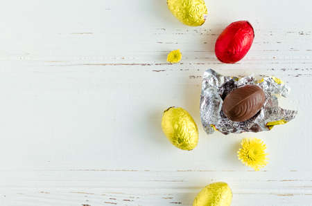 Easter composition with chocolate eggs with yellow flowers on white shabby chic wooden background with place for text. Copy space.の写真素材