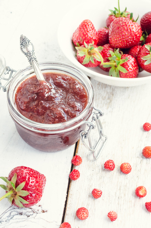 Homemade delicious strawberry jam in a glass jar and fresh strawberries on white rusric wooden background. Selective focus.の写真素材