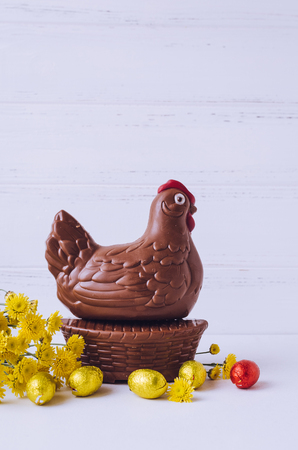 Easter composition with chocolate chicken in the nest and eggs with yellow flowers on white shabby chic wooden background with place for text. Copy space.の写真素材