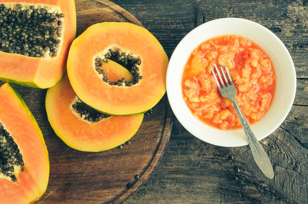 Fresh papaya natural facial mask peeling puree in white plate with fork on wooden background. Skin care and wellness vitamin antioxidant cosmetic concept. Top view.の写真素材