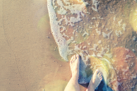Feet of a young woman touching water on tropical beach in sunny summer day. Vacation holidays concept. Top view. Copy space.の写真素材