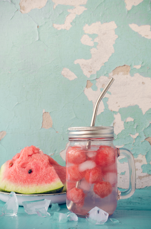 Watermelon drink in glass mason jar with slices of watermelon and ice on blue background with place for text. Summer fresh fruit flavored infused detox water. Copy space.の写真素材