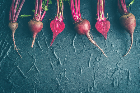 Row of homegrown organic young beets with green leaves on dark stone table. Food background. Concept of healthy eating. Toned image. Top view. Copy space.の写真素材
