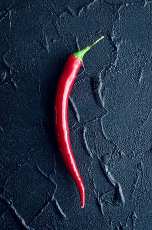 One red hot chili pepper over dark concrete background. Overhead view of chilli peppers on black stone table. Minimalism style. Top view.の写真素材