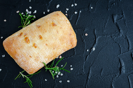 Freshly baked loaf of traditional italian bread ciabatta on black stone table with rosemary and...