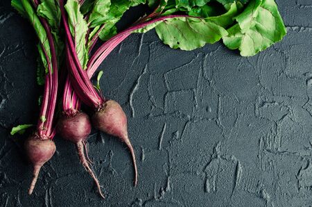 Pile of homegrown organic young beets with green leaves on dark stone table. Fresh harvested beetroots on black concrete background with place for text. Top view. Copy space.の写真素材