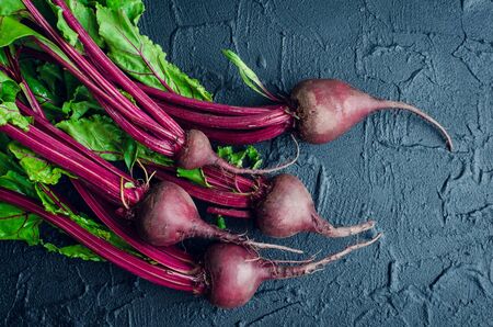 Pile of homegrown organic young beets with green leaves on dark stone table. Fresh harvested beetroots on black concrete background. Top view.の写真素材