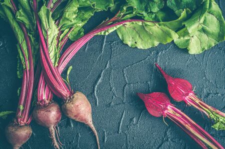 Pile of homegrown organic young beets with green leaves on dark stone table. Fresh harvested beetroots on black concrete background. Top view. Toned image.の写真素材