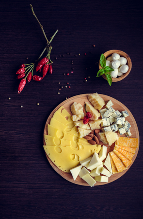 Cheese plate: Parmesan, cheddar, gouda, mozzarella and other with chili pepper and almonds on wooden board. Tasty appetizers. Top view.の写真素材