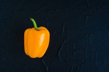 Orange yellow bell pepper over dark concrete background with place for text. Overhead view of fresh...