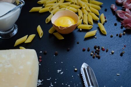 Ingredients for Pasta Carbonara on dark background. Set of products for pasta Carbonara - pasta, bacon, cream, Parmesan cheese, egg. Italian food concept. Selective focus.の写真素材