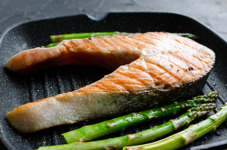 Grilled salmon steak and asparagus prepared on grill pan on black stone background. Healthy food concept. Close up.の写真素材