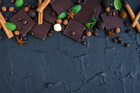 Dark chocolate with coffee beans candy covered with chocolate, cinnamon, anise and green mint leaves on black background. Top view. Copy space.の写真素材