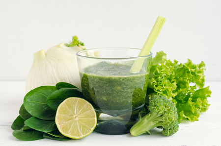 Detox green smoothie in a glass with ingredients: spinach, celery, lettuce, fennel, lime and broccoli on white wooden background. Dieting clean eating vegan fitness healthy lifestyle concept.の写真素材
