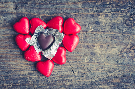 Valentines Day background with red chocolate heart shaped candies on a rustic wooden table with place for text. Romantic love concept. Valentine's greetings card. Copy space. Top view.の写真素材