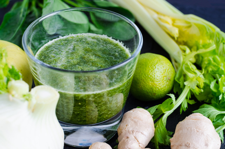 Detox healthy green smoothie in a glass on black background with ingredients: spinach, celery, ginger, fennel, lime and apple. Diet, health, clean eating vegetarian food concept.の写真素材