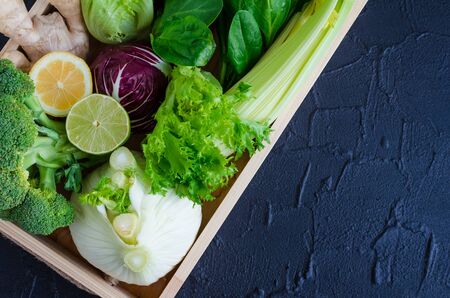 Assorted green and purple fresh vegetables, greens and fruit in wooden tray on black background. Detox dieting, clean eating, vegetarian, vegan, fitness, healthy lifestyle concept. Flat lay. Top view.の写真素材