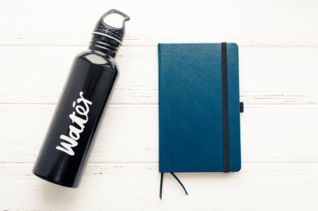 Black aluminum reusable water bottle and dark blue notebook on white shabby chic wooden background. Fitness, healthy and active lifestyles concept. Top view.の写真素材