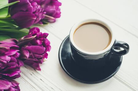 Coffee with milk and flowers tulip. Cup of coffee and purple tulips on white wooden table. Breakfast on Mothers day, Valentines Day or Womens day. Spring background.の写真素材