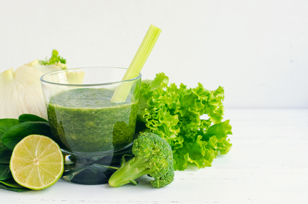 Green vegetable juice in a glass with ingredients: spinach, celery, lettuce, fennel, lime and broccoli on white wooden background. Dieting clean eating fitness healthy lifestyle concept. Copy space.の写真素材