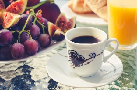 Breakfast table with coffee, a glass of fresh orange juice, a plate of the burgundy grapes, figs and...
